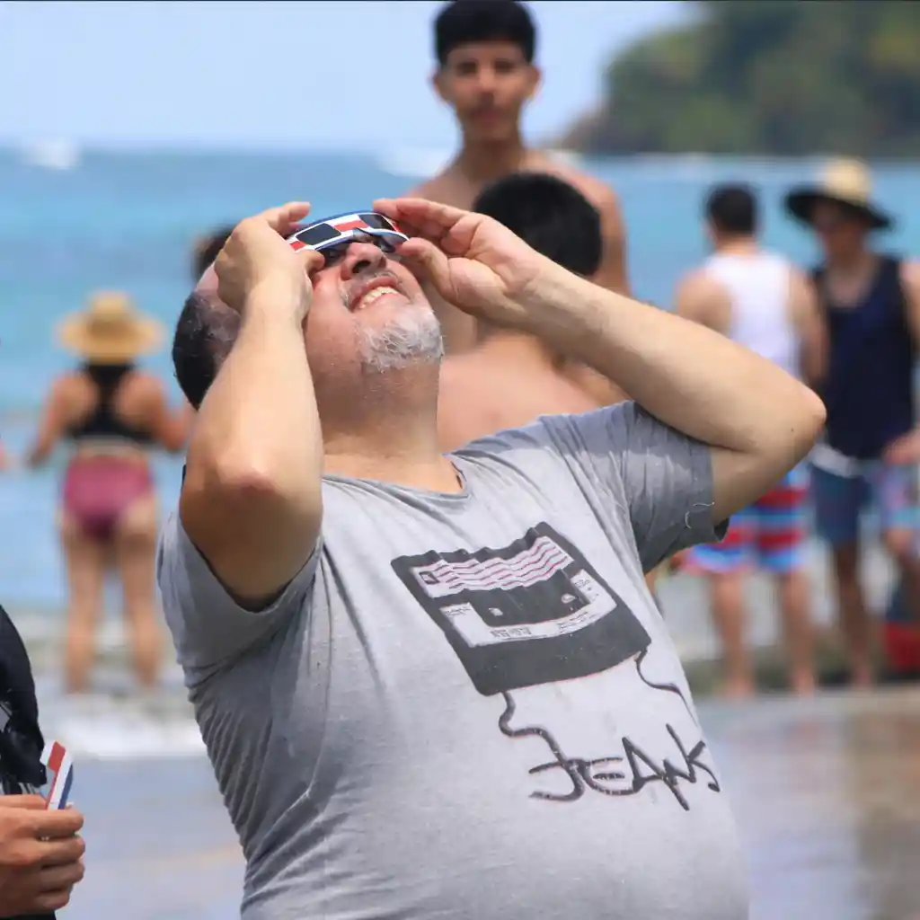 Persona che indossa occhiali per l’eclissi solare a tema Costa Rica in spiaggia.